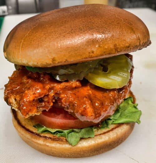 Juicy fried chicken sandwich with pickles, lettuce, tomato, and spicy sauce on a toasted bun. Perfect for burger lovers.